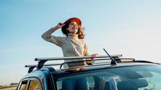 Cheerful young woman wearing hat enjoying through sun roof of car
