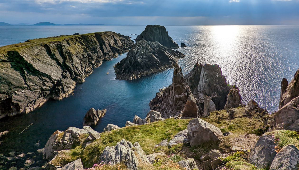 Airijos kraštovaizdžio scena su saulės šviesa, šviečiančia pro debesis virš uolėtų uolų ir vandenyno Malin Head Airijoje