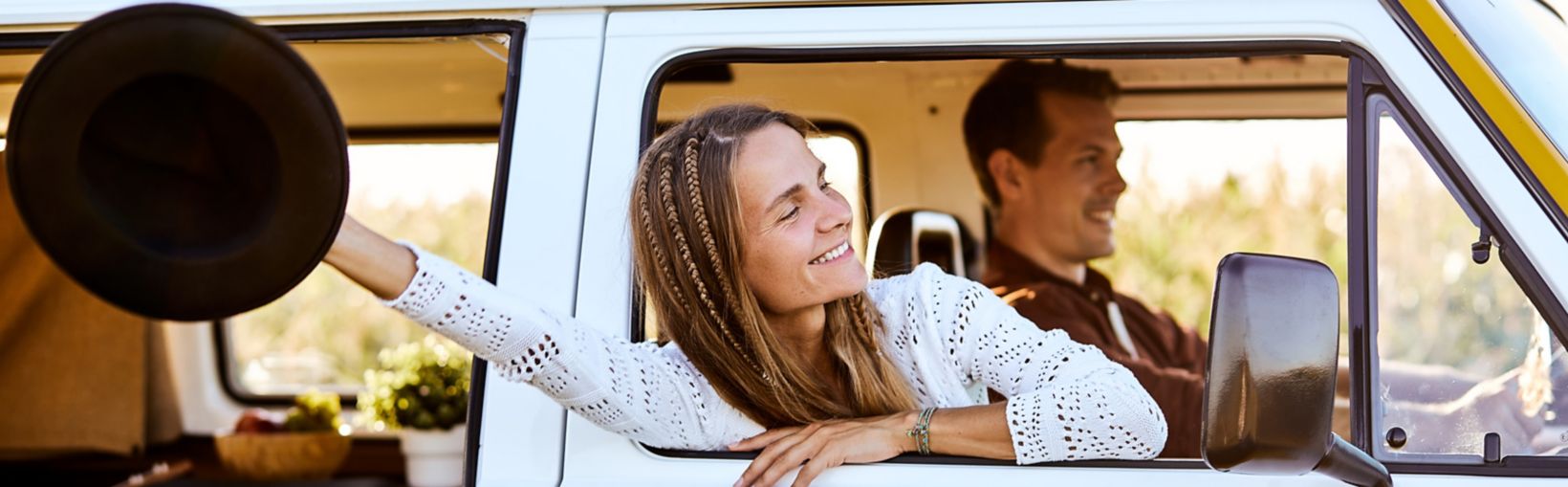 Happy beautiful caucasian young woman looking and smiling out of window from old yellow vintage van bus, in countryside. travel driving concept for cute attractive pretty female with long hair.