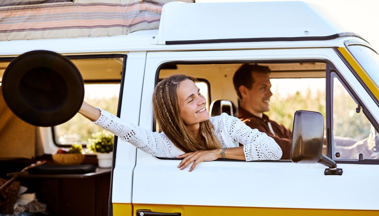 Happy beautiful caucasian young woman looking and smiling out of window from old yellow vintage van bus, in countryside. travel driving concept for cute attractive pretty female with long hair.