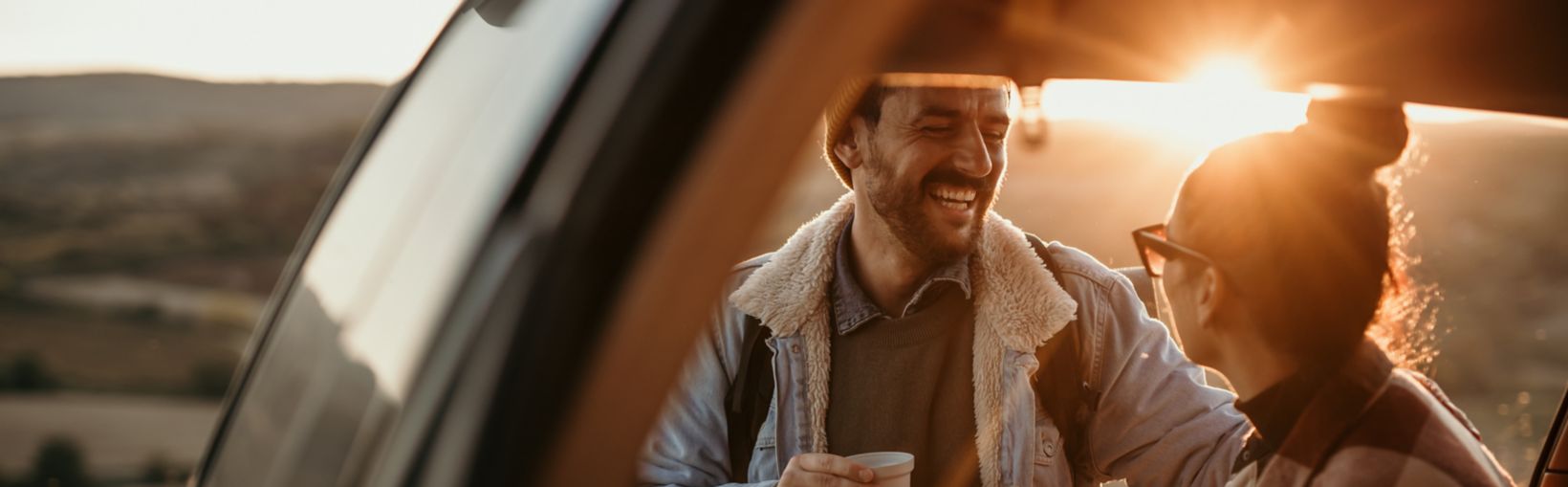 Couple travelling, talking, drinking a coffee watching the sunset from their car. 