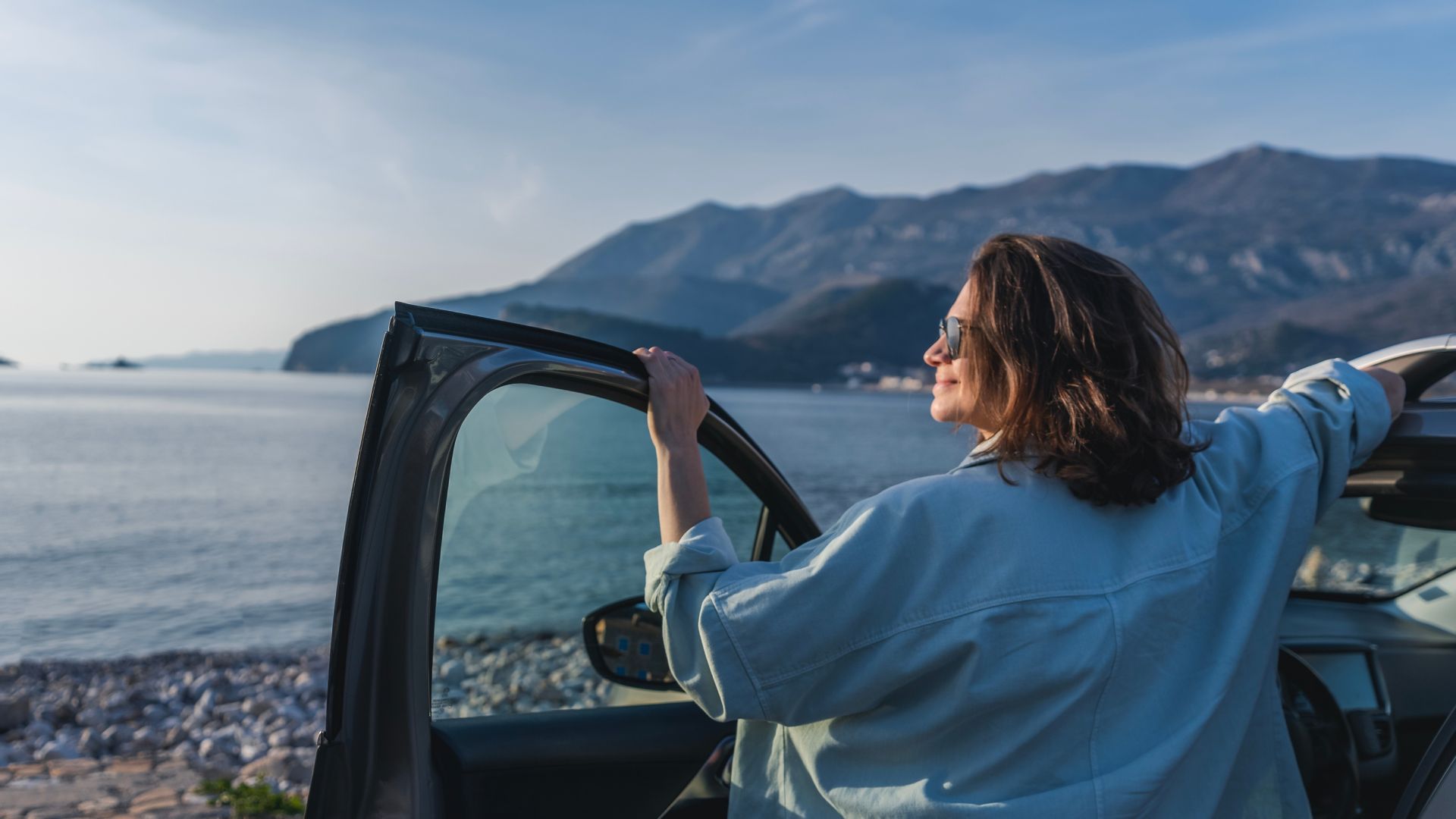 Young happy woman traveler enjoying the sunset at the sea while standing next to the car. Summer holidays and travel concept