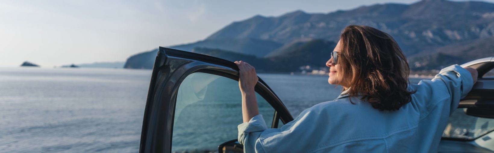 Young happy woman traveler enjoying the sunset at the sea while standing next to the car. Summer holidays and travel concept