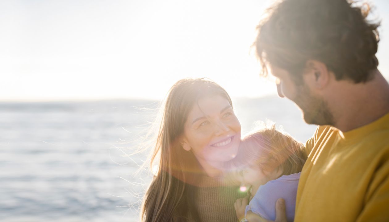 Smilende kvinne ser på en mann som holder datteren på stranden en solskinnsdag.