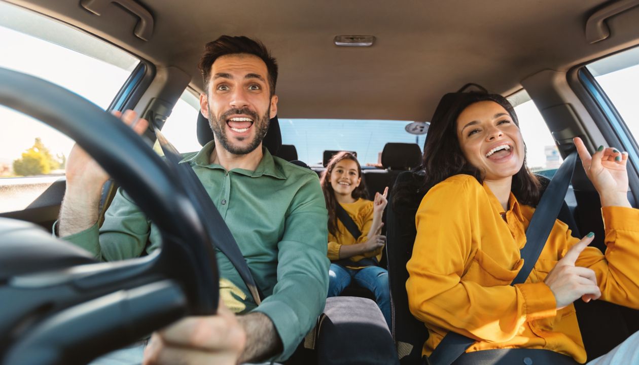 We are going on vacation. Happy family of three driving in their automobile, dancing to music and singing
