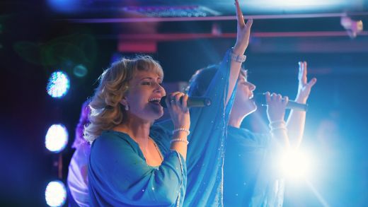 Trzech mężczyzn śpiewających z entuzjazmem karaoke z piosenkami ABBA podczas rejsu Stena Line, w radosnej atmosferze imprezy na pokładzie.
