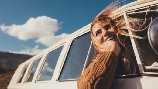 Woman driving a van and enjoying road trip. Laughing young female having fun on her vacation.