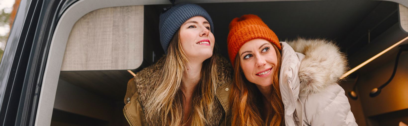 Smiling women with long hair wearing knit hats sitting in motor home