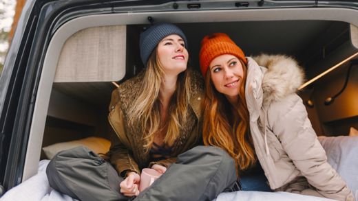 Smiling women with long hair wearing knit hats sitting in motor home