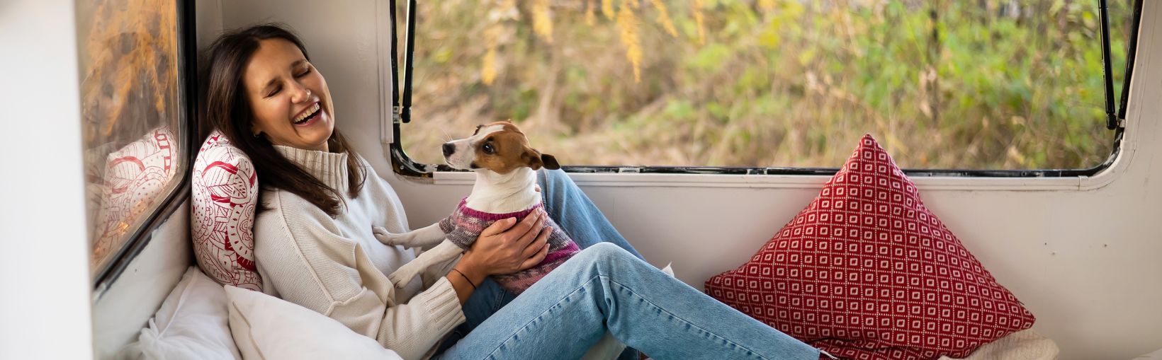 Caucasian woman sitting in a van hugging with dog Jack Russell Terrier. Travel in a camper in the fall