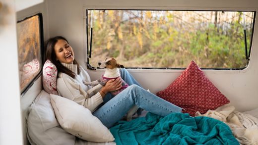 Caucasian woman sitting in a van hugging with dog Jack Russell Terrier. Travel in a camper in the fall