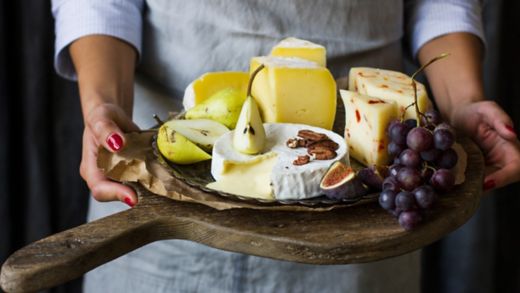 Kvinna håller ett fat med ostar plus päron plus vindruvor plus fikon plus nötter