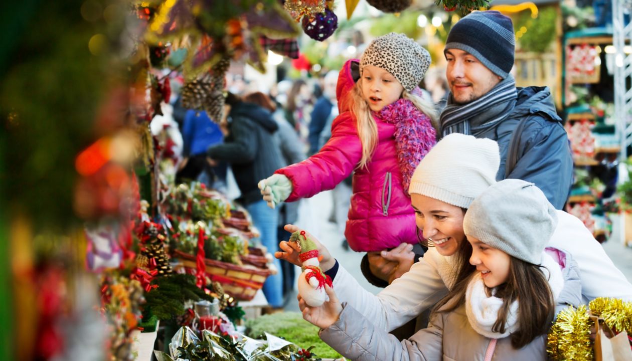 Family with little girls standing at coniferous Christmas souvenirs counter. Focus on women 