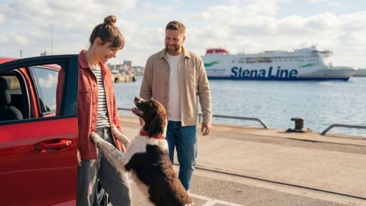 Couple with dog by car on quayside, Stena Line ferry behind, ready for pet-friendly travel