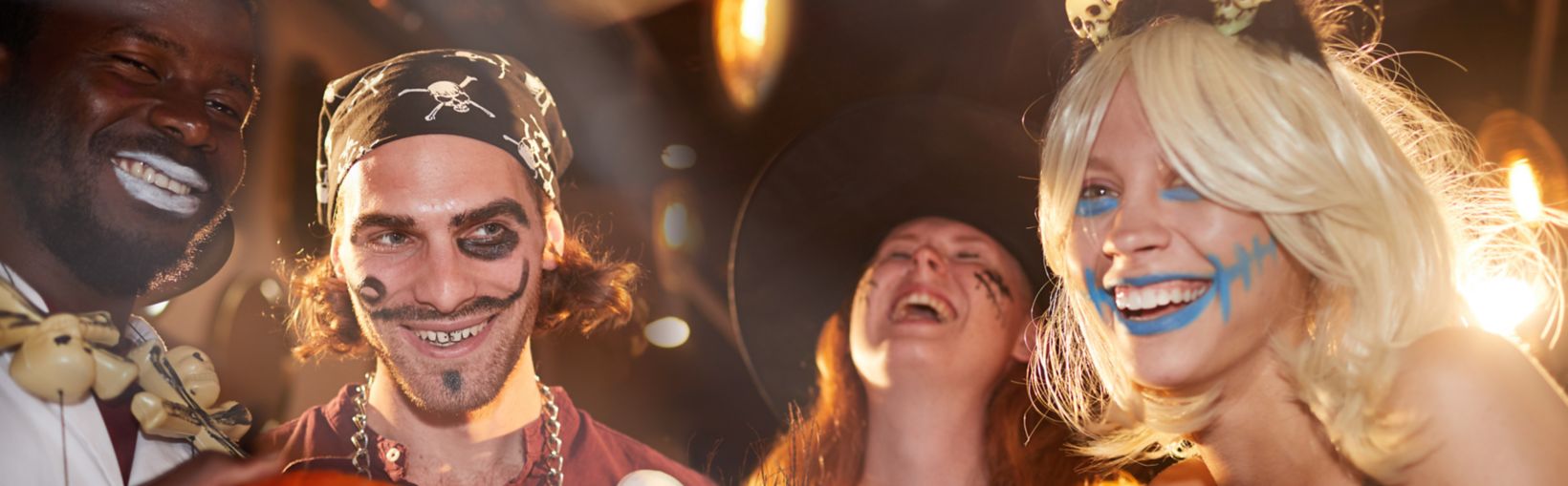 Grupa przyjaciół w halloweenowych kostiumach śmieje się razem na imprezie, trzymając dynię i kwiaty, świętując jesień.