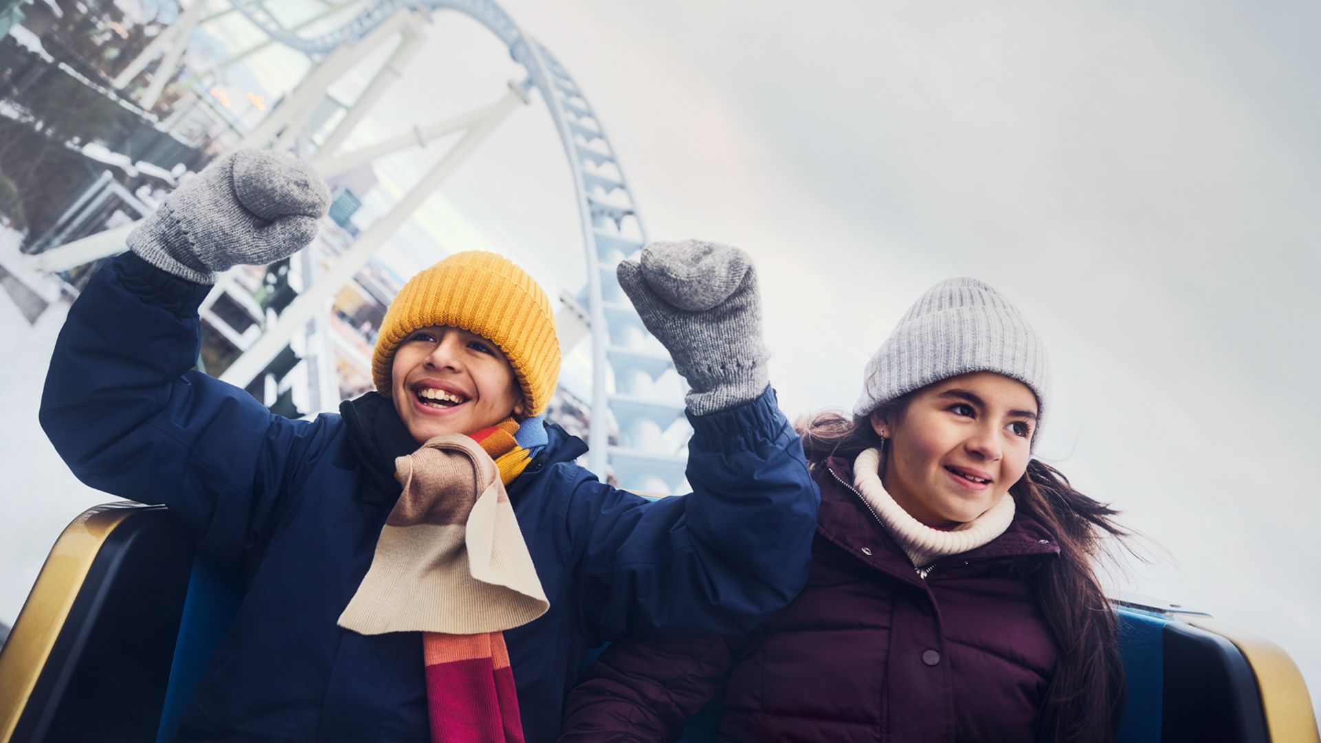Two children enjoy a winter roller coaster ride at Liseberg, smiling with arms raised against a snowy backdrop