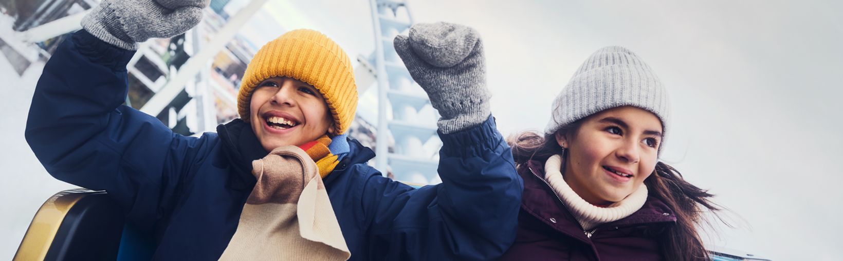 Two children enjoy a winter roller coaster ride at Liseberg, smiling with arms raised against a snowy backdrop