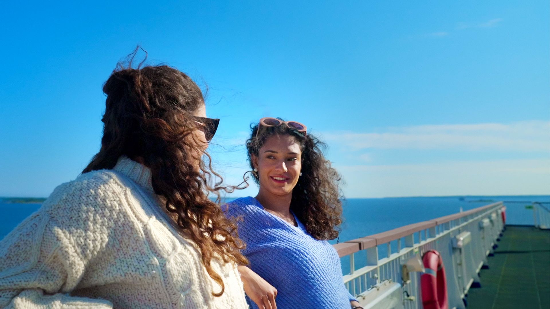 Two women smiling and chatting on the sunny deck of a Stena Line ferry, enjoying a relaxing sea journey.