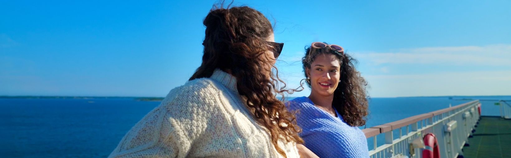 Two women smiling and chatting on the sunny deck of a Stena Line ferry, enjoying a relaxing sea journey.