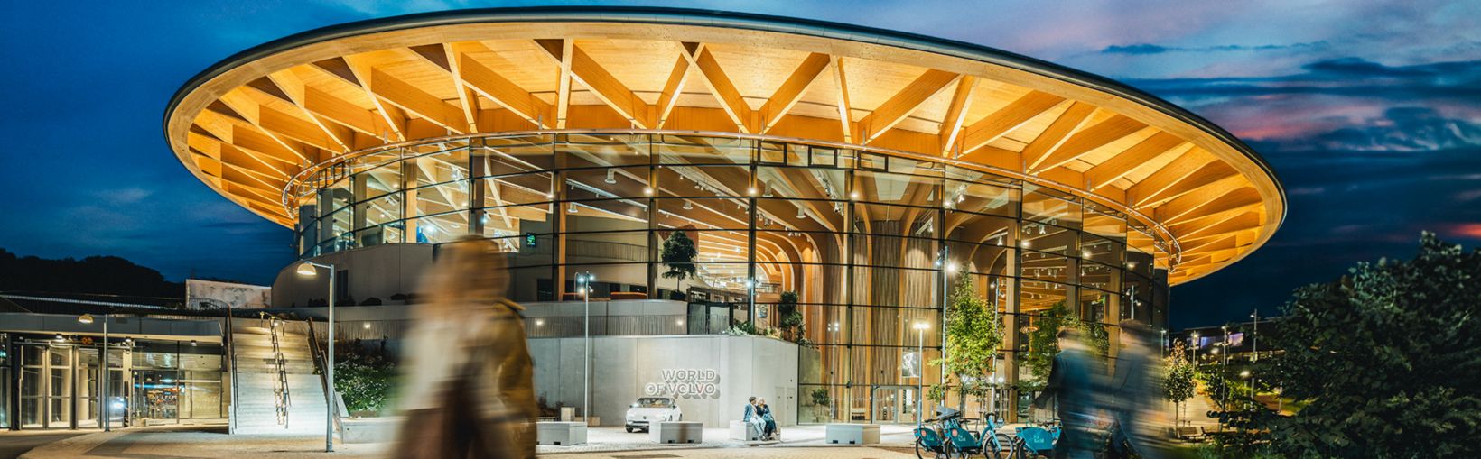 Ein modernes, architektonisch gestaltetes Gebäude mit großen Glasfenstern und einem geschwungenen Holzdach.