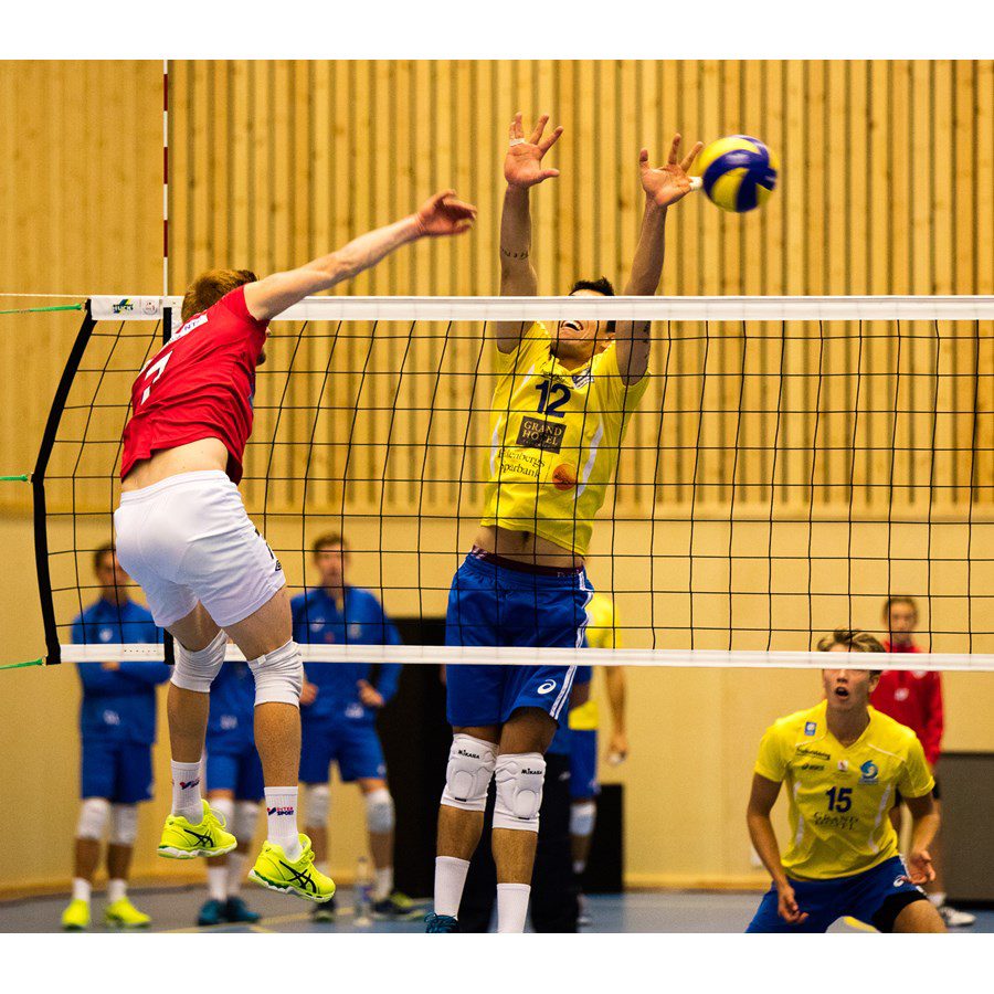 Volleybollspelare från olika lag möts i ett hopp vid nätet i jakt på bollen.