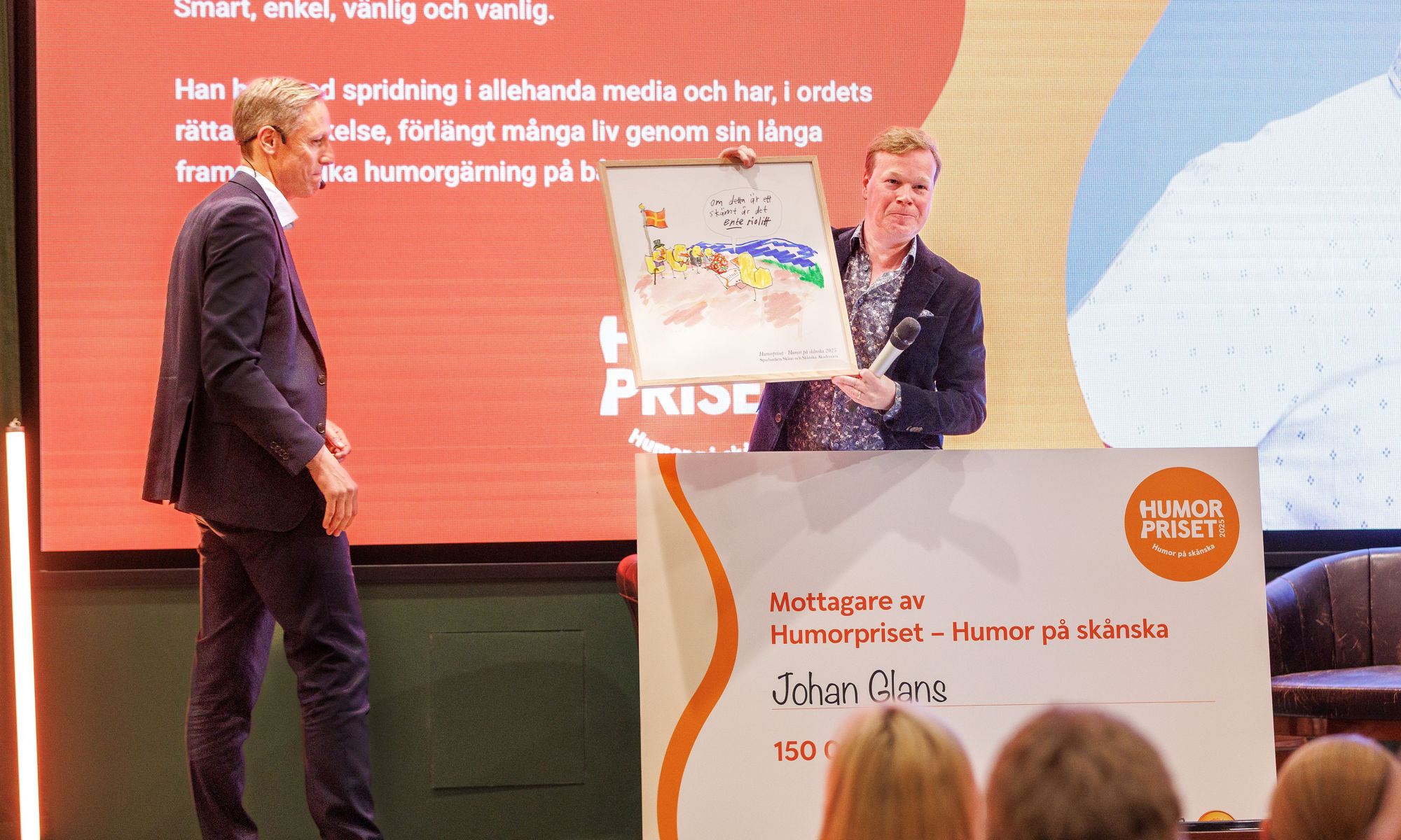 Rasmus Roos and Johan Glans at the stage recieving the price Humorpriset 2025 holding up a painting. 