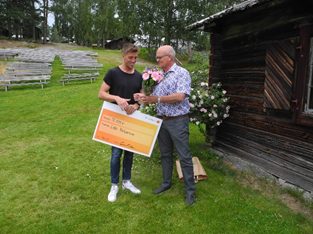 Prisutdelning för Årets Bjursing. Två män står utanför ett hus varav den ena tar emot priset.