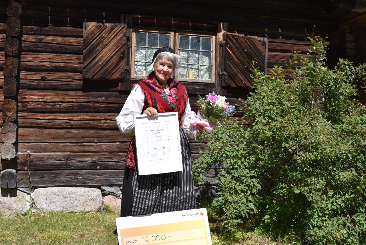 Leende kvinna i folkdräkt har tagit emot en blombukett och ett pris för årets Bjursing
