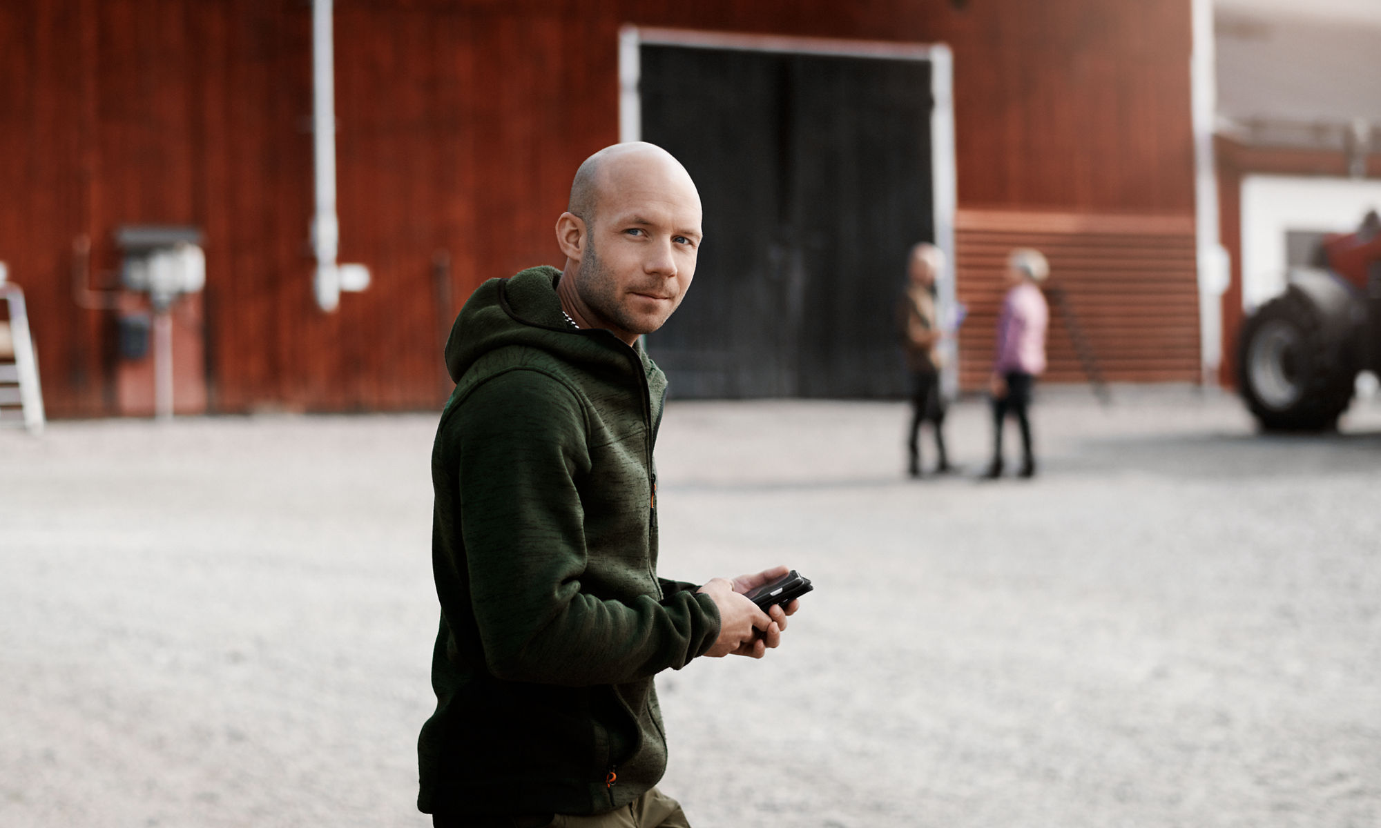 Man på en gård som tittar in i kameran med en mobil i händerna.