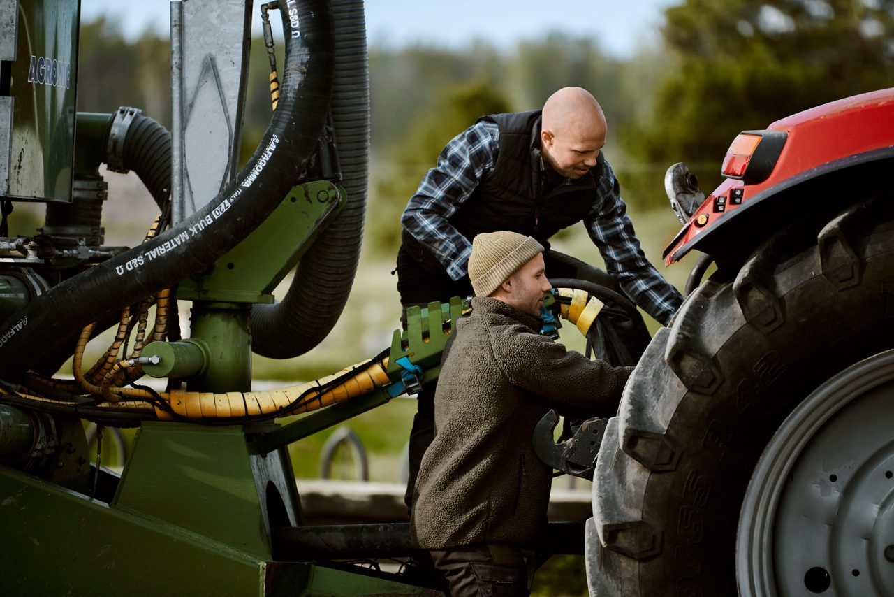 Två män som kopplar en jordbruksmaskin till en traktor.