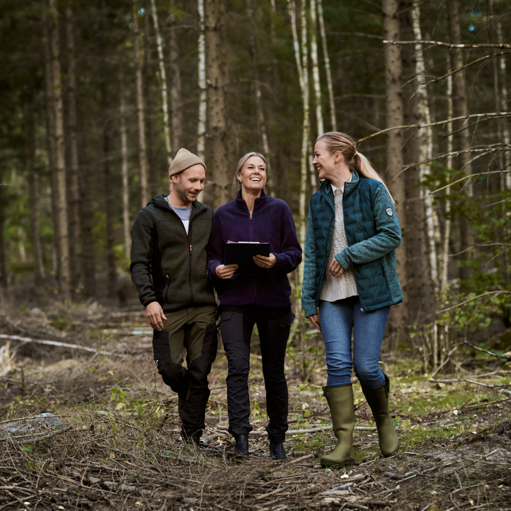 Två kvinnor och en man i arbetskläder i skogen.