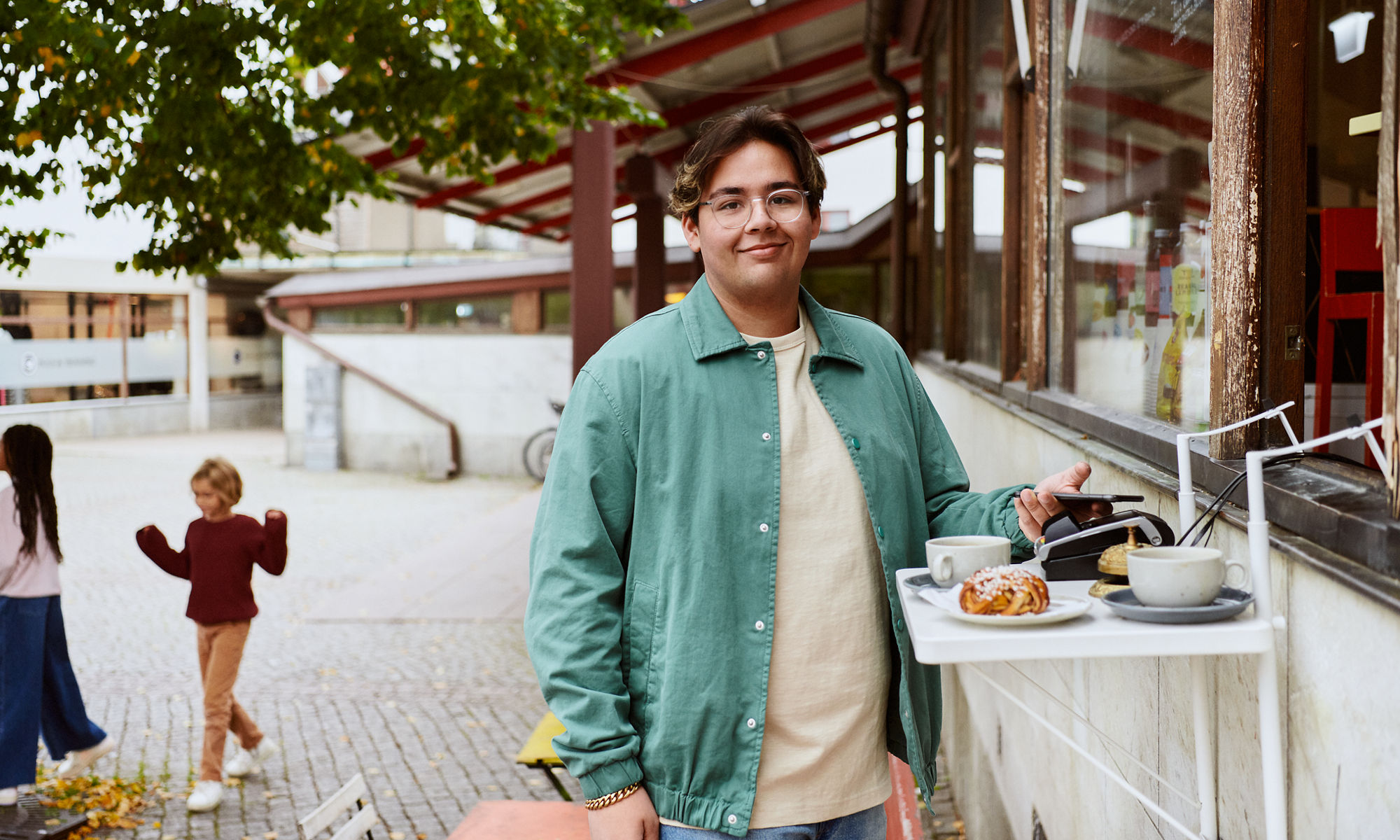 Ung man som använder sin telefon för att betala för kaffet på ett utomhuskafé.