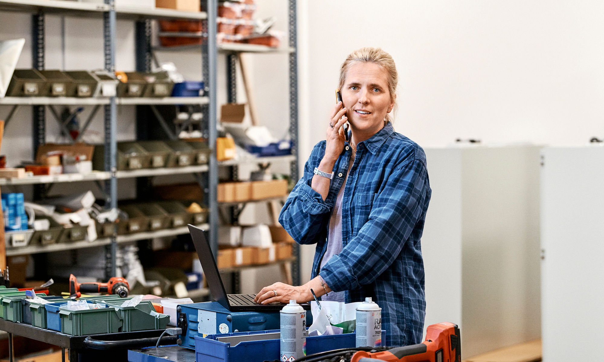 Kvinna som pratar i telefon vid en arbetsbänk i ett lager.