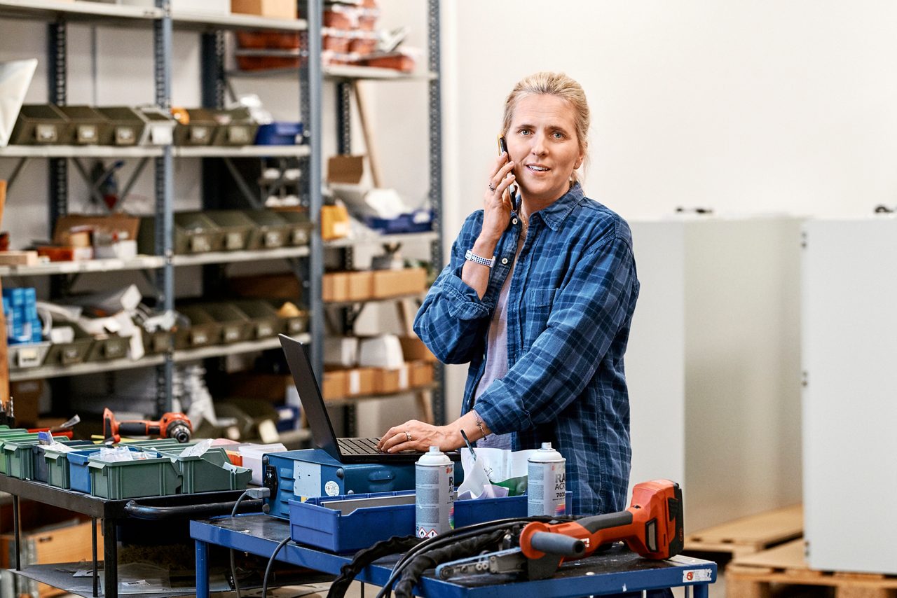 Kvinna som pratar i telefon vid en arbetsbänk i ett lager.