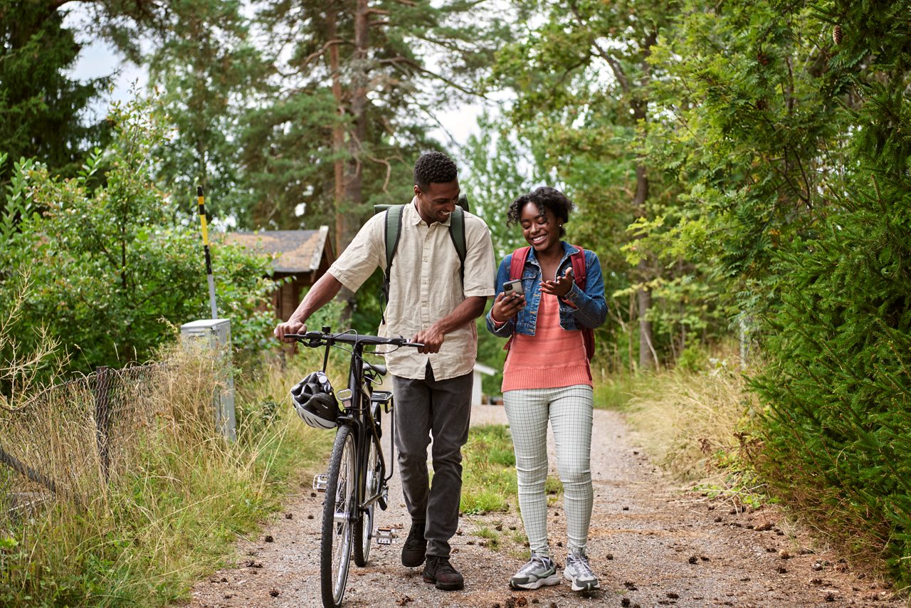 Ung kvinna och man med en cykel som går på en grusväg.
