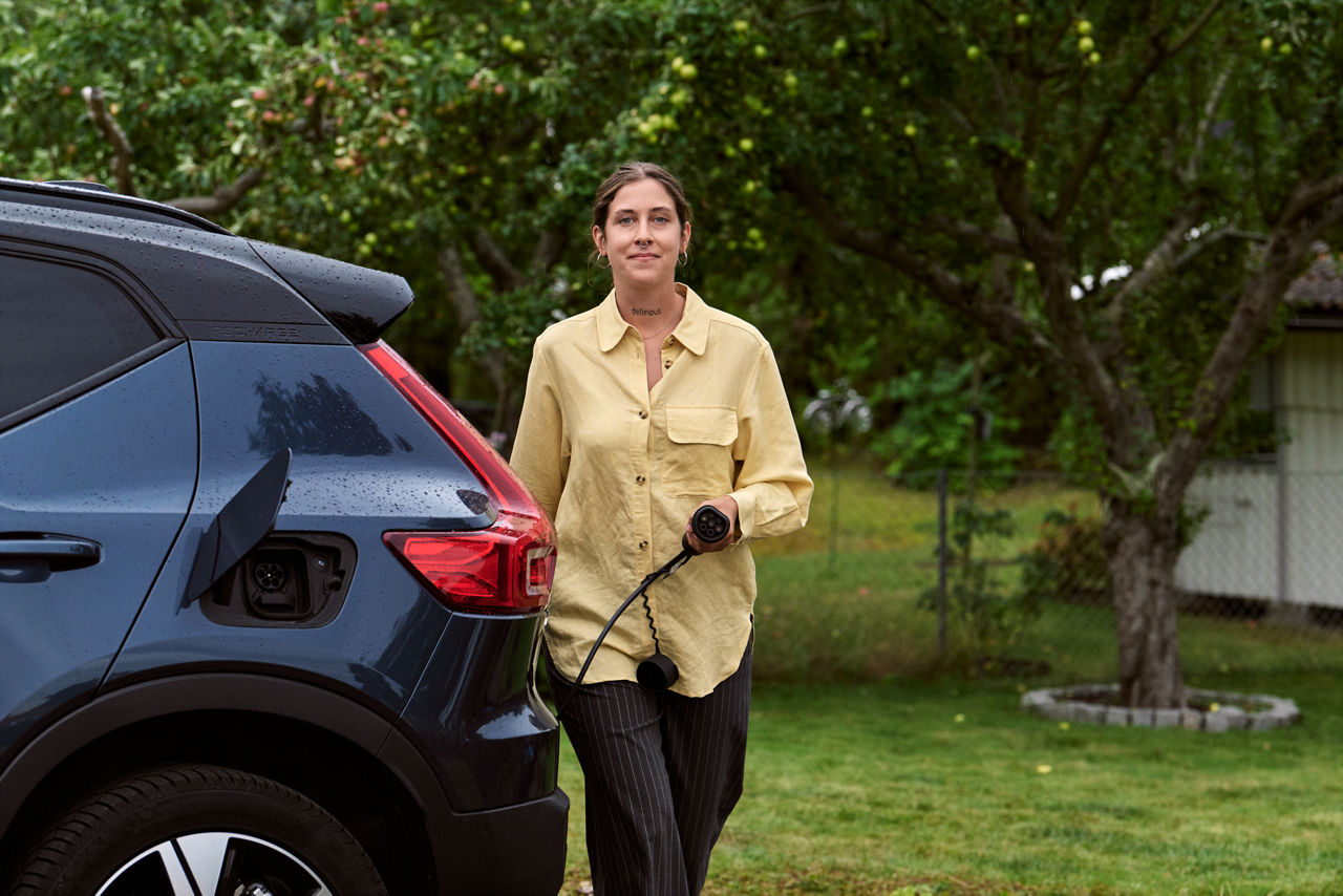 En kvinna med en laddkabel bakom en elbil.