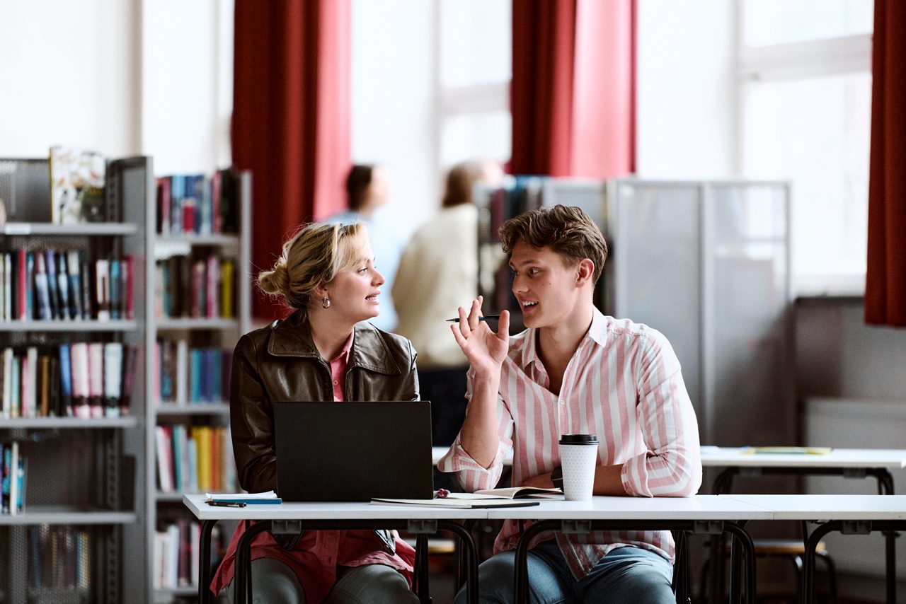 Studenter sitter och diskuterar och studerar tillsammans i ett bibliotek