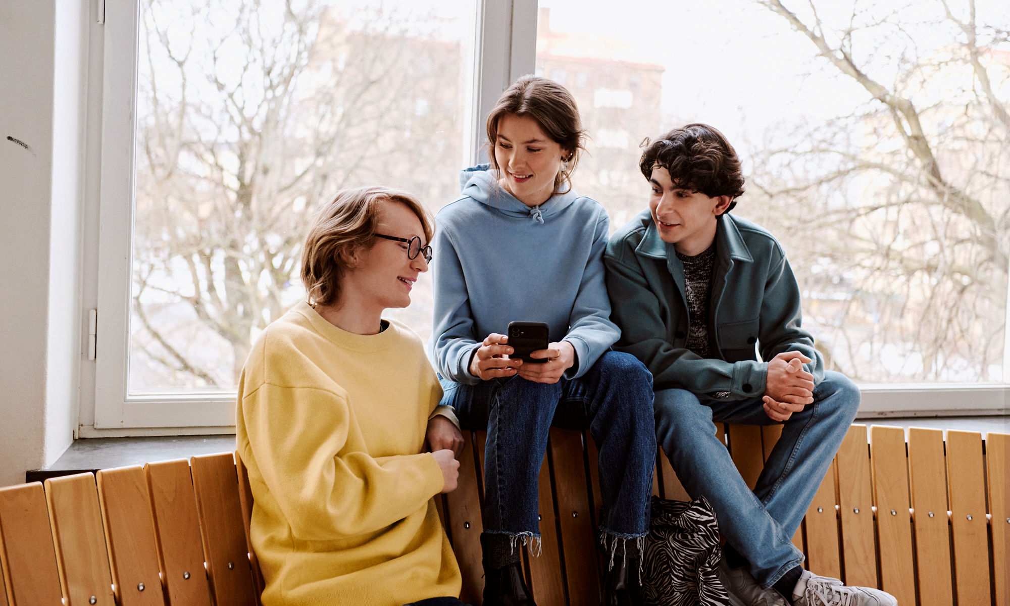 Studenter sitter och pratar på en bänk, en av dem håller i en mobiltelefon