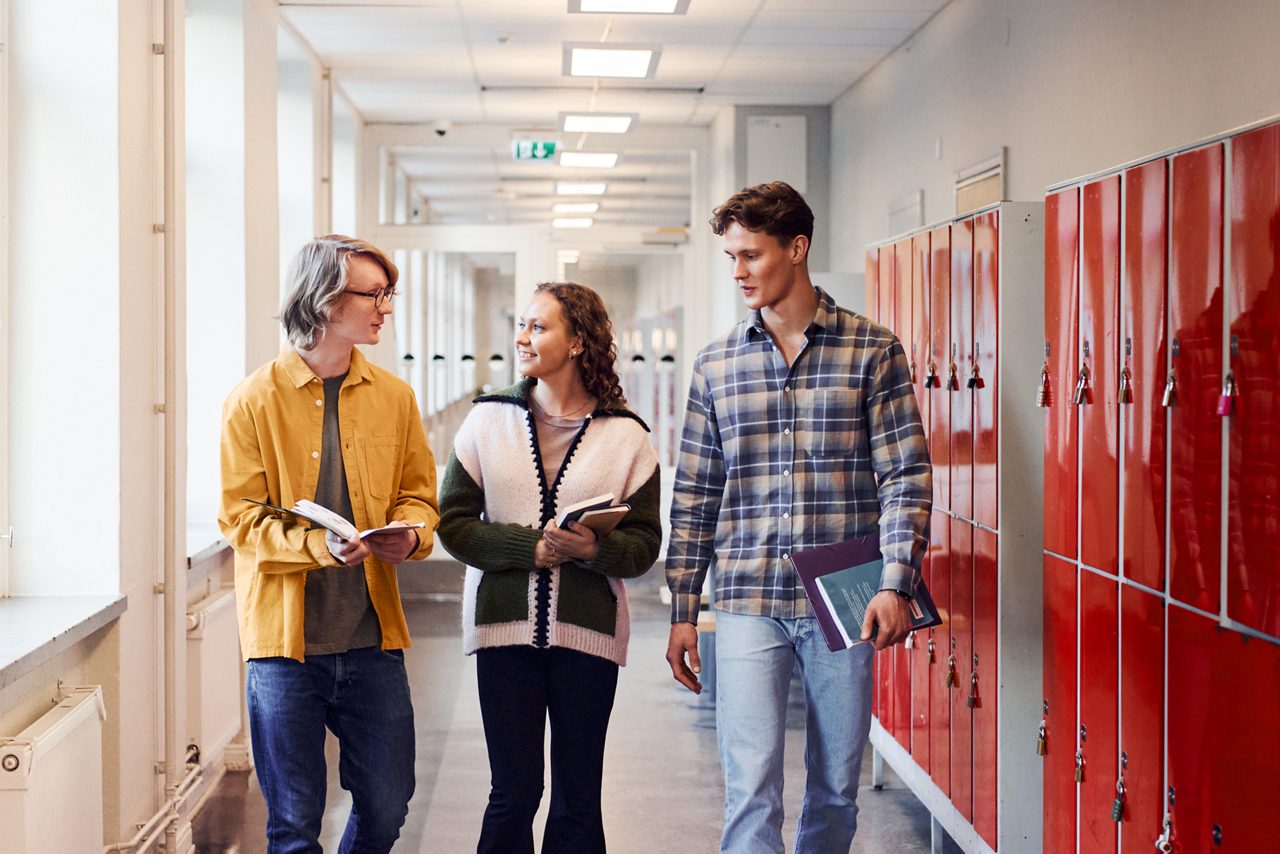 Tre studenter går och pratar i skolkorridoren