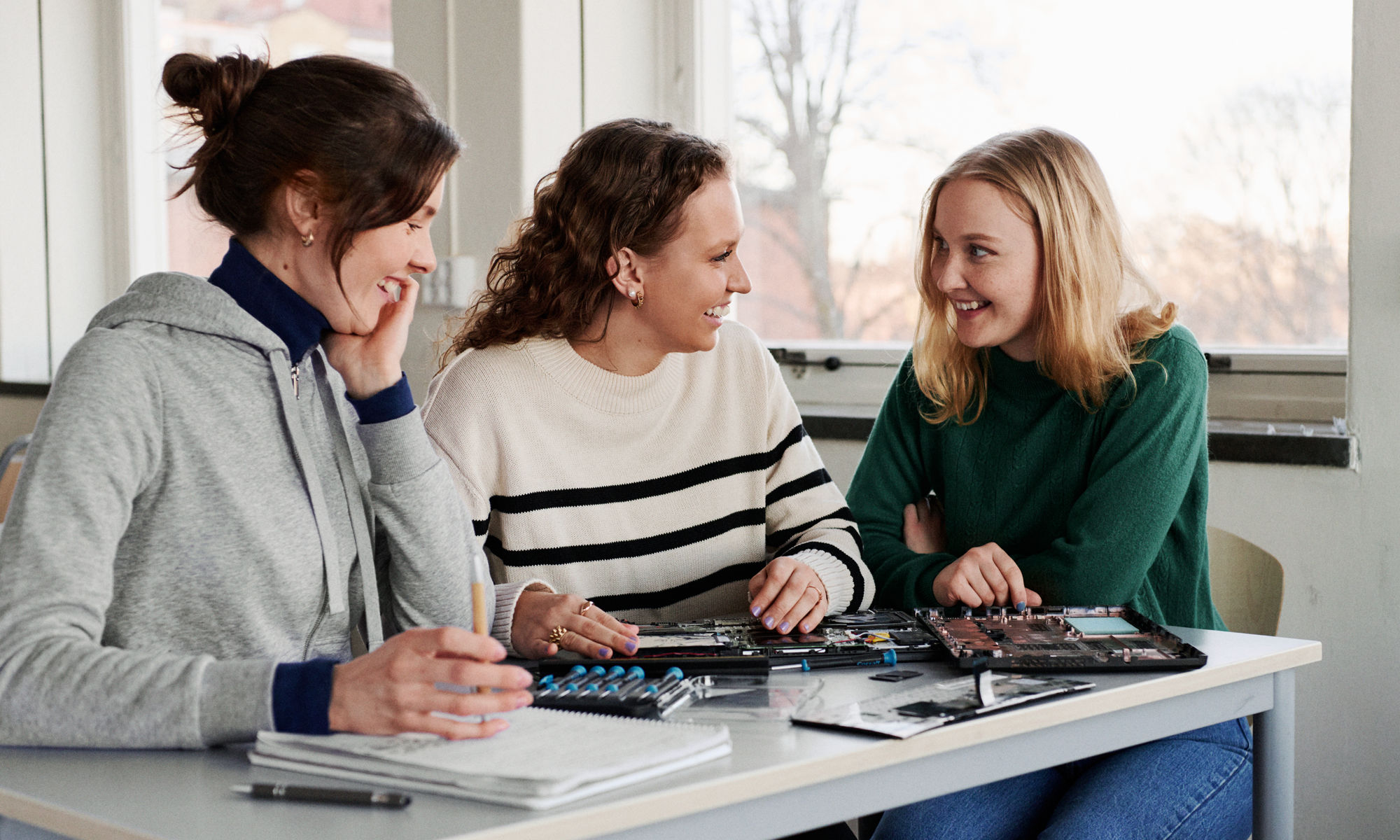 Tre kvinnliga studenter sitter och pratar under en lektion