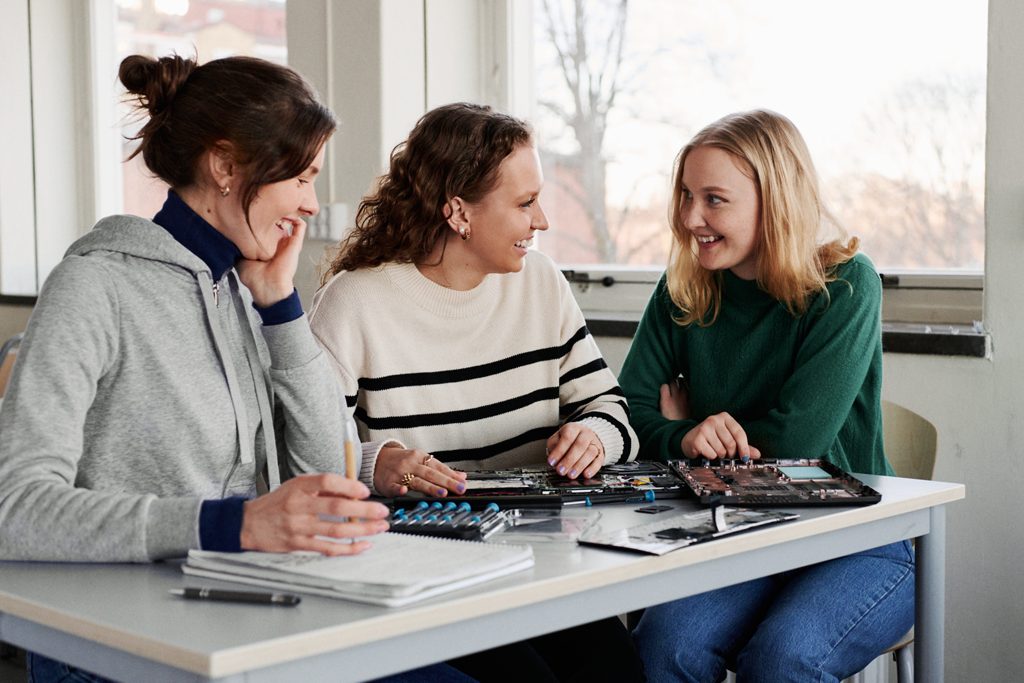 Tre kvinnliga studenter sitter och pratar under en lektion