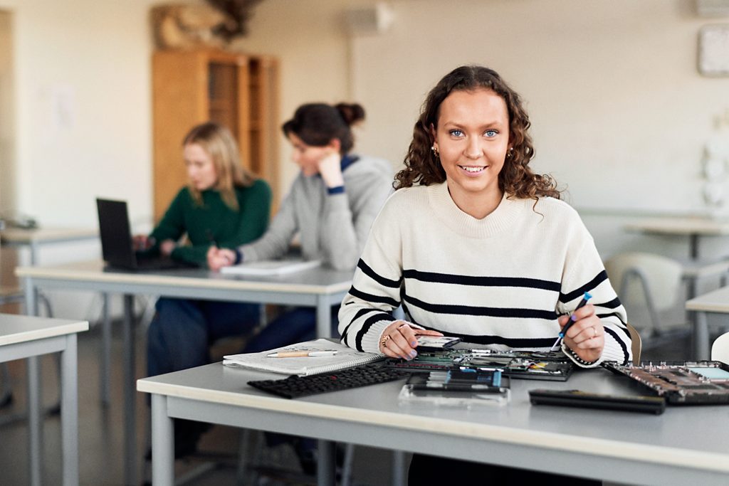 En kvinnlig student har tekniklektion i ett klassrum, ler mot kameran