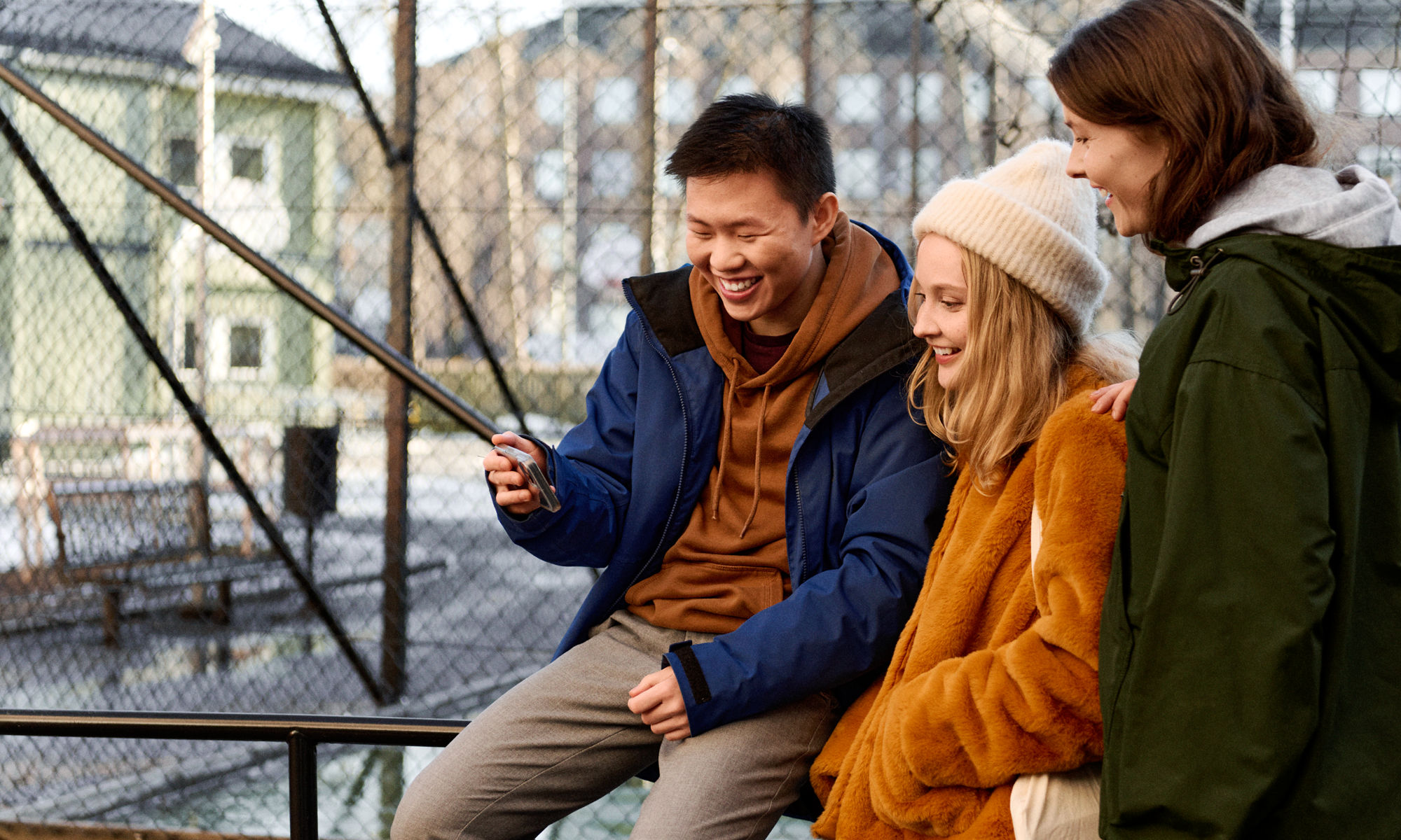 Tre studenter hänger på skolgården, tittar på en mobiltelefon och skrattar