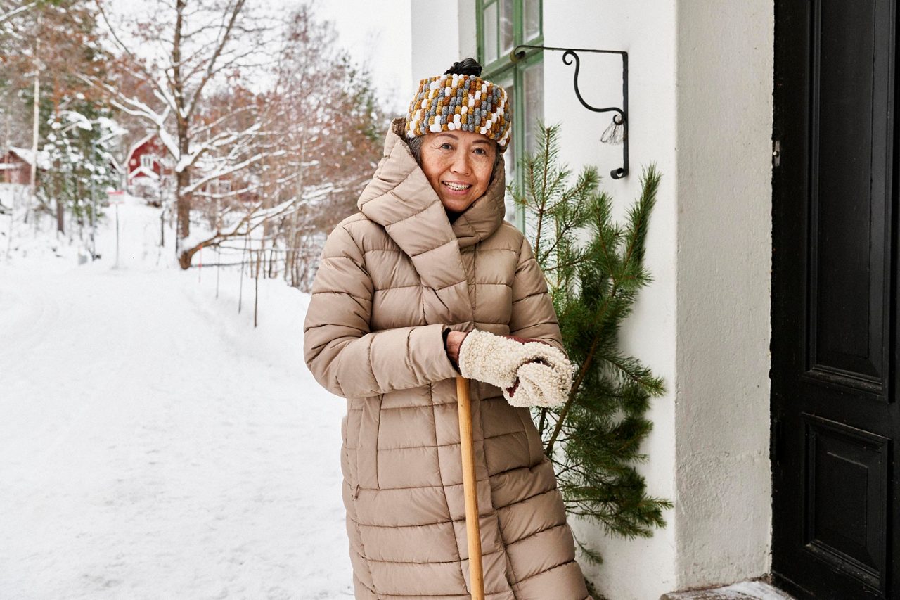 Äldre kvinna står utanför ett dörr med en snöskyffel