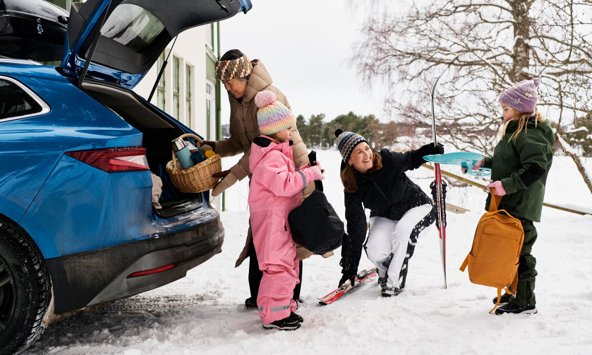 Vuxna och barn packar en bil med picknickkorg och skidor
