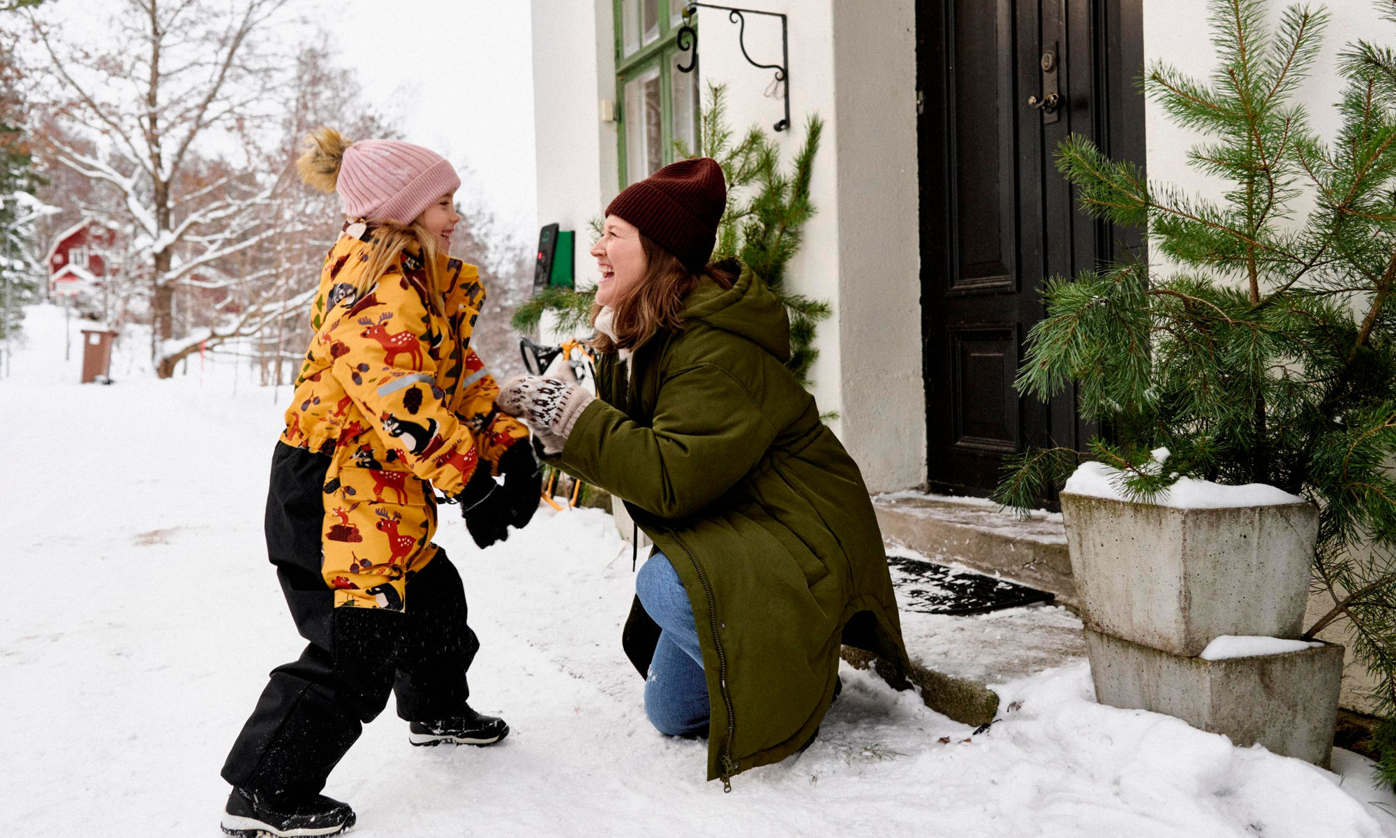 En kvinna och ett barn skojar i snön utanför ett hus