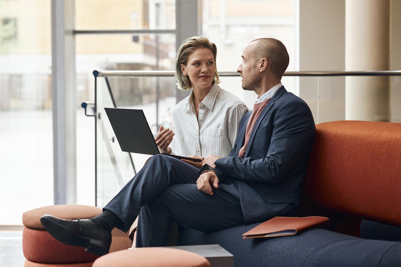 En kvinna och en man sitter i ett möte på en soffa i en kontorsmiljö