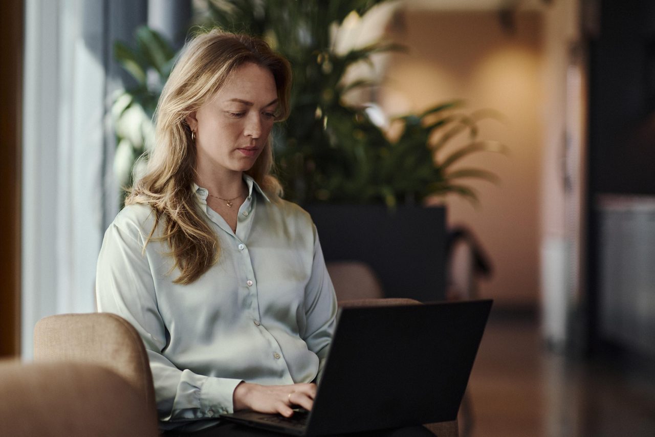 En kvinna sitter i en fotölj och använder en bärbar dator