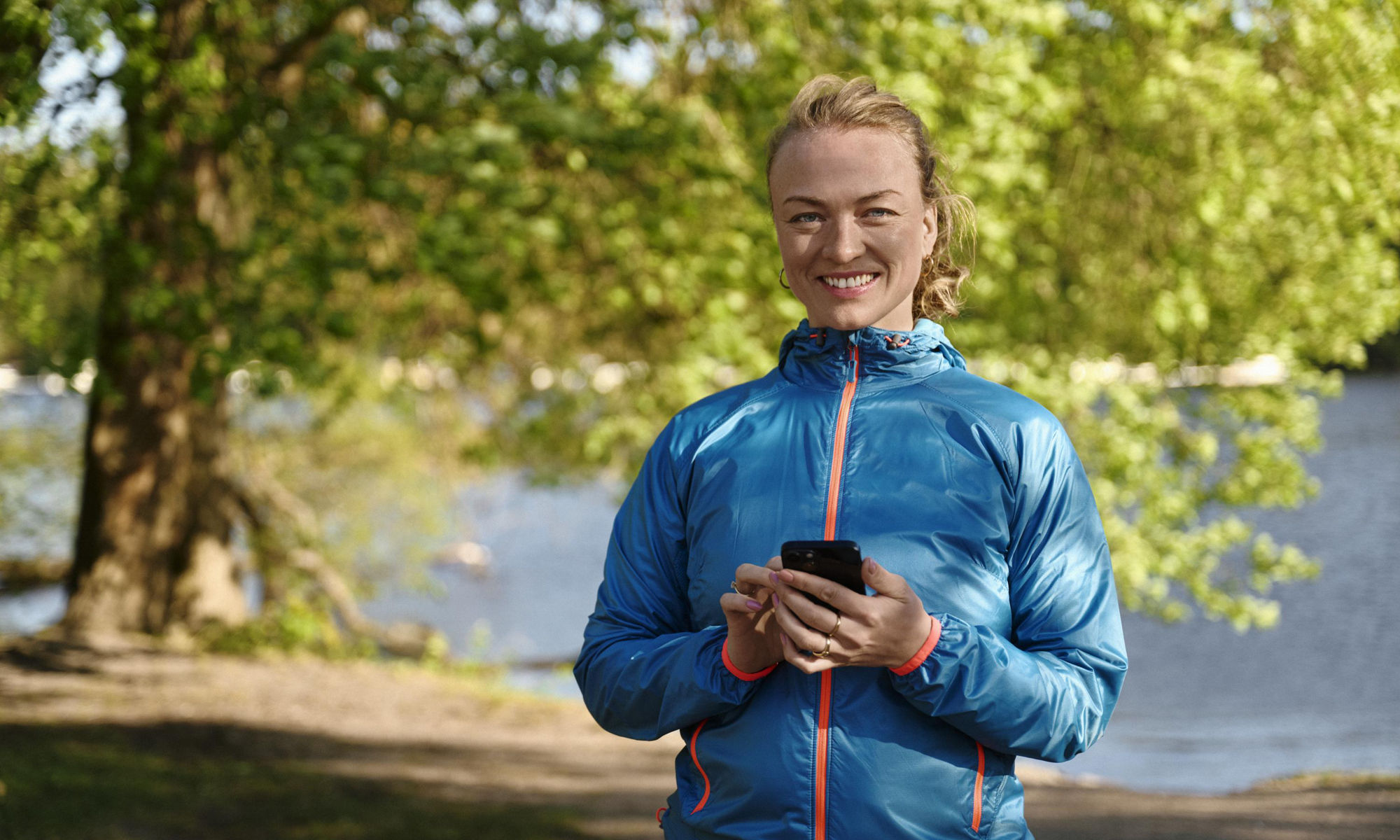 Träningsklädd kvinna står och håller i en mobiltelefon