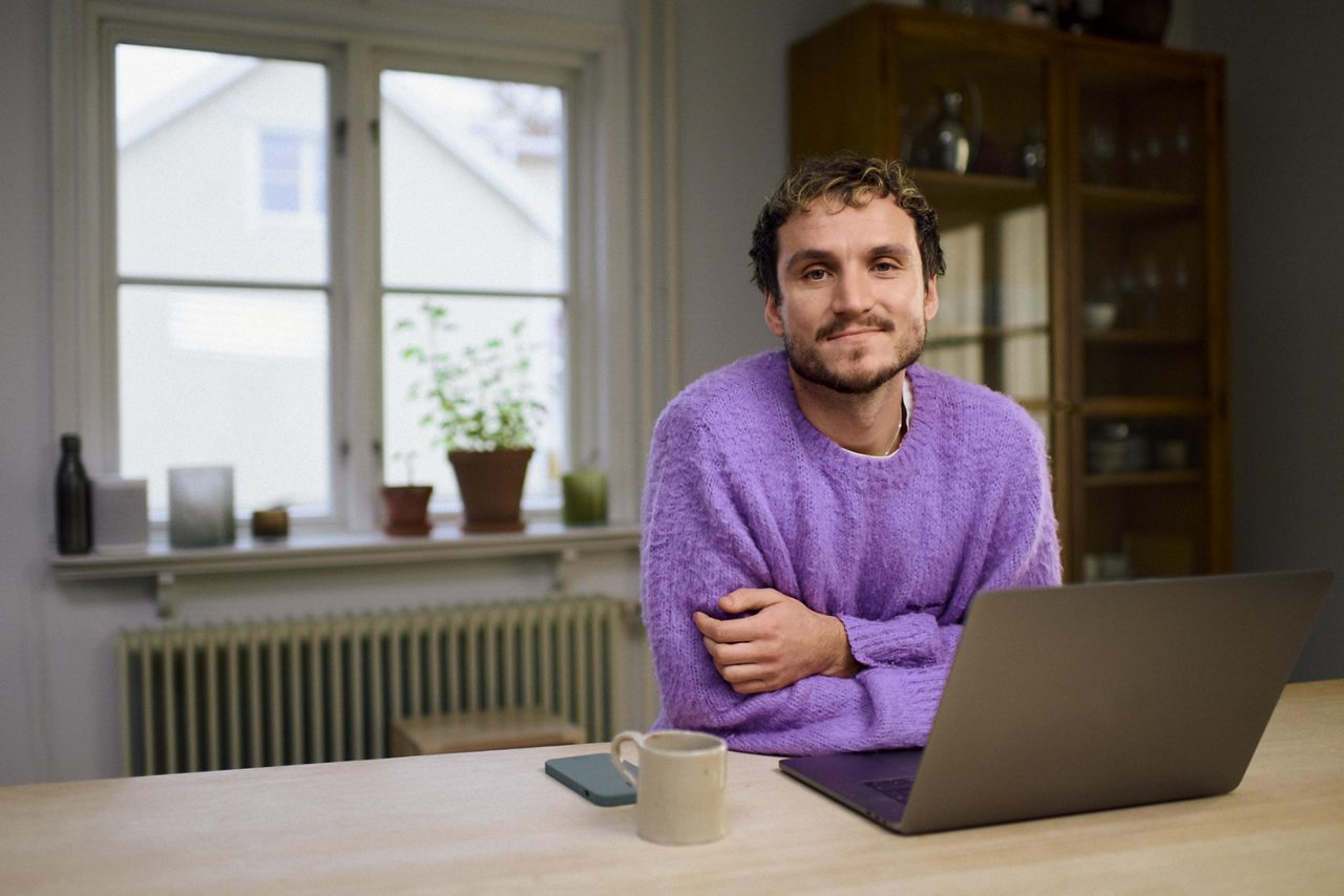 En man använder en laptop vid ett köksbord.